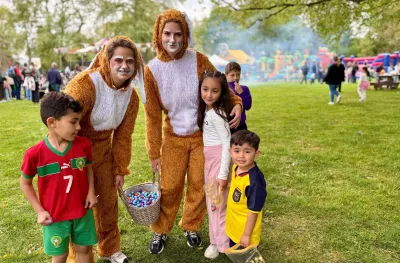 Kinderen poseren met twee paashazen die een mand vol chocolade eitjes vasthouden