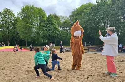 Kinderen spelen in het zand, oma met kindje op de arm wuift naar de paashaas