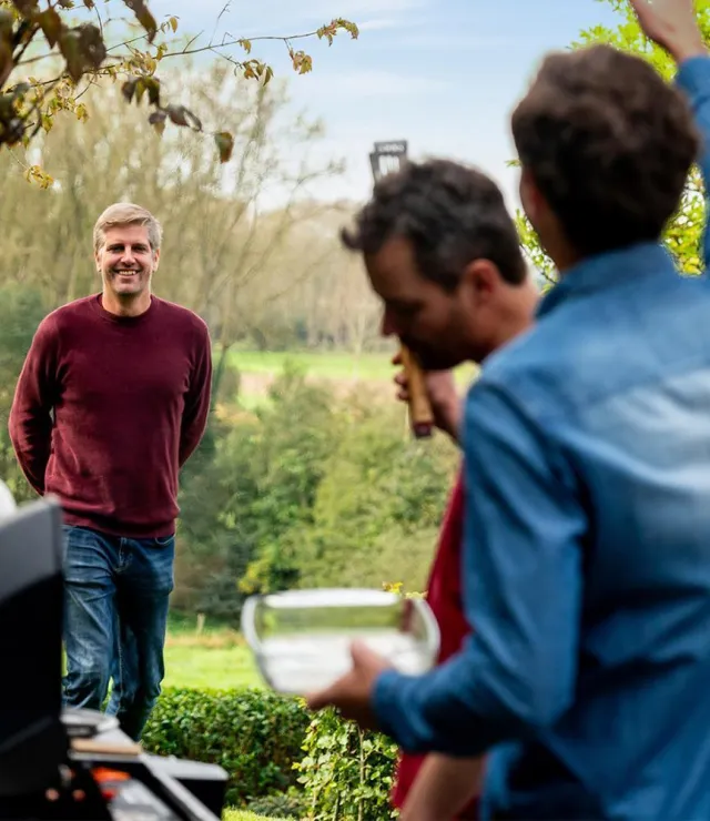 2 vrienden aan een BBQ-toestel die zwaaien naar een derde vriend