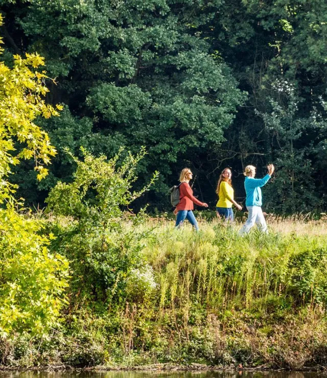 3 vrouwen op wandel naast het water, er staan bomen in de achtergrond