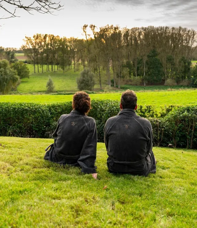 Een man en een vrouw in badjes zitten op het gras en kijken naar een groene omgeving