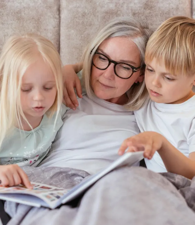 Grootmoeder leest met haar kleinkinderen in een boekje onder een fleecedeken